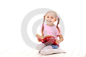 Joyful little girl with books sits on a white floor.