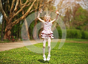 Joyful little girl child jumping from happiness in spring green park