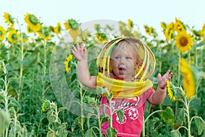 A joyful little girl dressed in a beekeepers mask waves her hands against the background of a field with sunflowers. Beekeeping