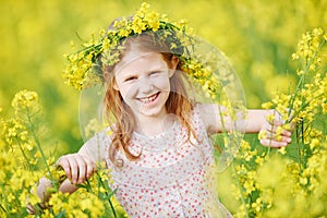 Joyful little girl with flower garland at yellow meadow