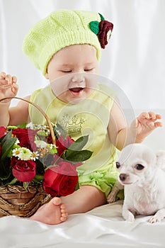 Joyful little girl in greenish clothes and hat sits on bedding