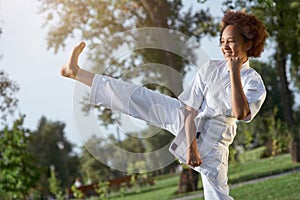 Joyful little girl in kimono practicing karate on the street