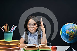 Joyful little girl sitting at the table with pencils and books textbooks. Happy child pupil doing homework at the table