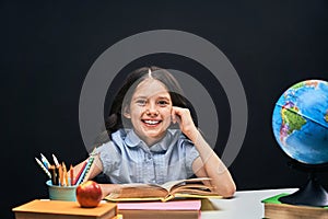 Joyful little girl sitting at the table with pencils and books textbooks. Happy child pupil doing homework at the table