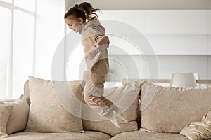 Joyful little kid girl in comfortable loungewear jumping on sofa. photo