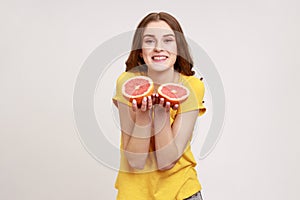 Joyful lively bright teenager girl wearing casual style attire showing half slice grapefruit to