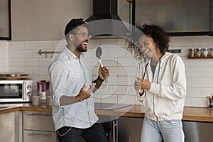 Happy young african american couple singing songs in kitchen.