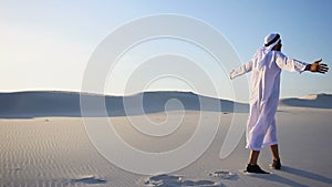 Joyful male Arabian Sheikh Muslim walks through white sand desert and enjoys life on sunny summer day.