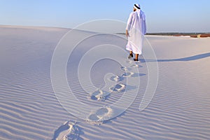 Joyful male Muslim walks through white sand desert and enjoys li