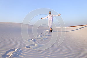 Joyful male Muslim walks through white sand desert and enjoys li