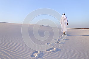 Joyful male Muslim walks through white sand desert and enjoys li