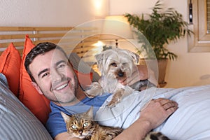 Joyful man in bed with a dog and a cat