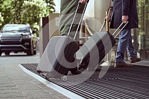 Joyful man in a cloak and his elegant wife arriving at a hotel with their luggage