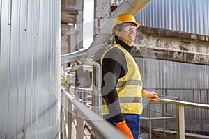 Cheerful male engineer standing near metal pipe at factory