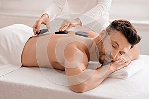 Joyful man having hot stone massage at luxury spa