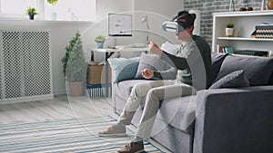 Joyful man moving arms sitting on couch wearing virtual reality glasses at home