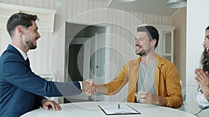 Joyful man signing sale and purchase agreement getting keys from broker shaking hands hugging wife