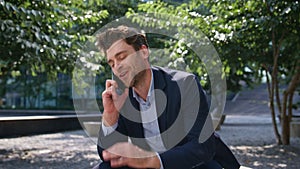 Joyful man speaking cell phone sitting sunny green street close up. Man calling