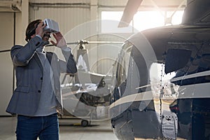 Joyful man in VR goggles standing near hangared helicopter photo