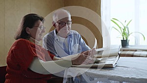 Joyful married couple old men and women rejoice and laugh enjoying family memories looking at photos in photo album