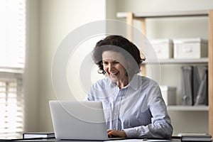 Joyful middle aged woman looking at laptop screen.