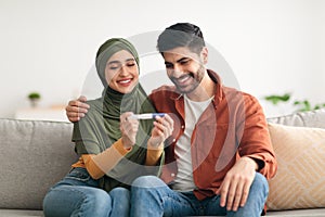 Joyful Middle Eastern Couple Holding Positive Pregnancy Test At Home