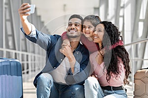 Joyful Middle Eastern Family Of Three Taking Selfie With Smartphone In Airport
