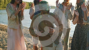 Joyful Middle Eastern man covered with gulal paint dancing with friends outdoors at beach party