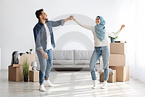 Joyful middle-eastern man and woman dancing in new apartment