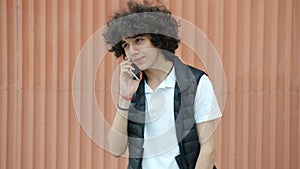 Joyful Middle Eastern teenager talking on mobile phone laughing standing outdoors