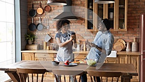 Joyful millennial black couple have fun at kitchen singing aloud