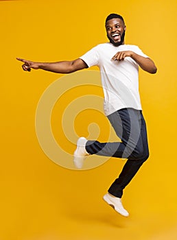 Joyful millennial guy jumping on air and pointing aside