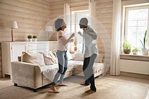 Joyful mixed race family spouse dancing in wooden living room.