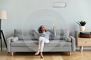 Joyful mixed race woman turning on cooler system air conditioner.