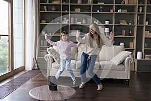 Joyful mom and happy active little girl dancing at home