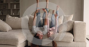 Joyful mom and little daughter lying upside down on sofa