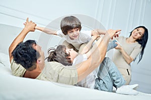 Joyful moments. Portrait of cute little latin boy having fun, playing with his parents and sibling, lying together on a