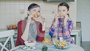 Joyful mother and cheerful daughter have fun grimacing silly with vegetables and looking into camera while cooking in
