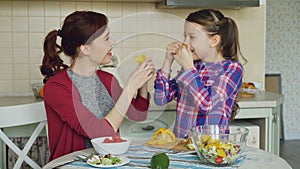 Joyful mother and cute cheerful daughter have fun grimacing silly with vegetables while cooking in the kitchen at home