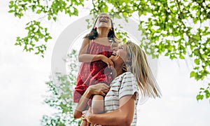 Joyful mother playing and riding on her shoulder her daughter in the park. Happy kid having fun with her mom enjoying the time