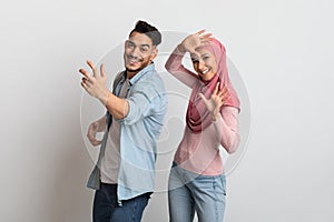 Joyful Muslim Couple Having Fun Together On Grey Background, Dancing And Laughing