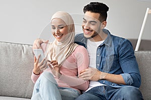 Joyful muslim couple watching photos on mobile phone together