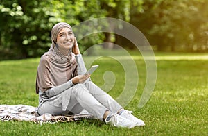 Joyful muslim girl listening to music, using smartphone