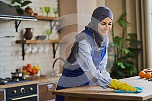 Joyful Muslim woman cleaning a table in the kitchen