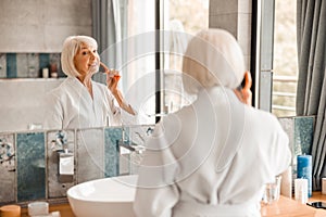 Joyful old lady looking in the mirror and brushing hair