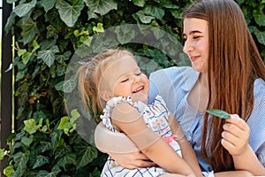 Joyful older sister holding younger sister, playing and laughing, having fun. Teen girl holding baby girl on summer day