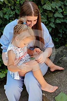 Joyful older sister holding younger sister, playing and laughing, having fun. Teen girl holding baby girl on summer day