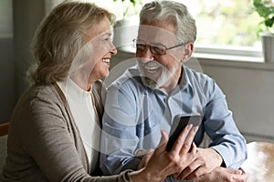 Joyful older spouses embrace relax with cell discuss funny video