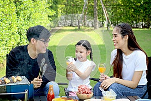 Joyful parent and kid child make barbecue at picnic party, have fun together in summer green garden, father mother and daughter