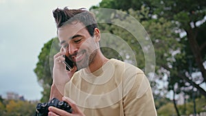 Joyful photographer speaking mobile phone in park close up. Man looking photo